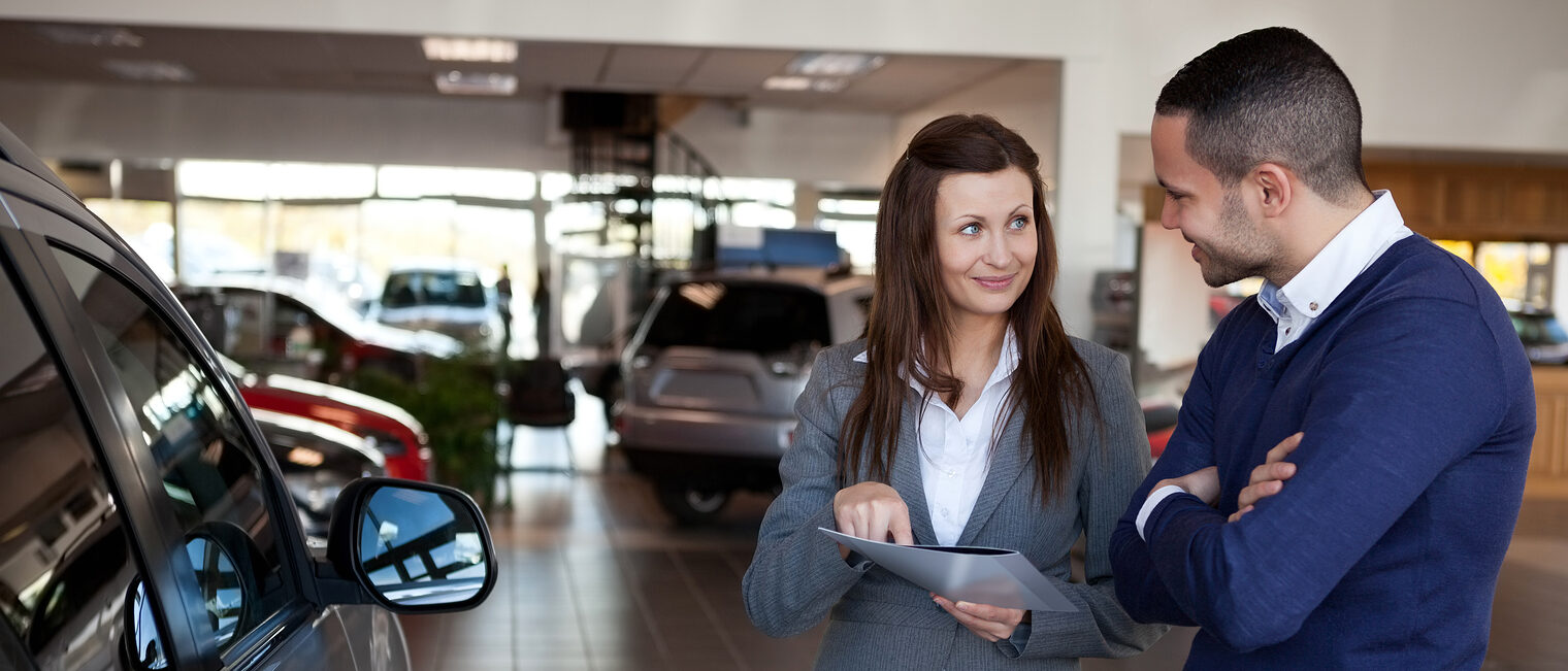 Woman explaining something to a man in a dealership Schlagwort(e): 20s, Young Adult, Man, Male, Mixed-Race, Woman, Female, Caucasian, Indoors, Businesswoman, Suit, Well Dressed, Smart, Elegant, Classy, Stylish, Sophisticated, Communication, Explaining, Interaction, Happy, Smiling, Dealership, Seller, Car, Dealer, Renter, Renting, Garage, Buyer, Vehicle, Automotive, Consumer, Client, Customer, Folder, File, Brunette, Brown Hair, Brunet, Standing, Holding, Showing, Clipboard