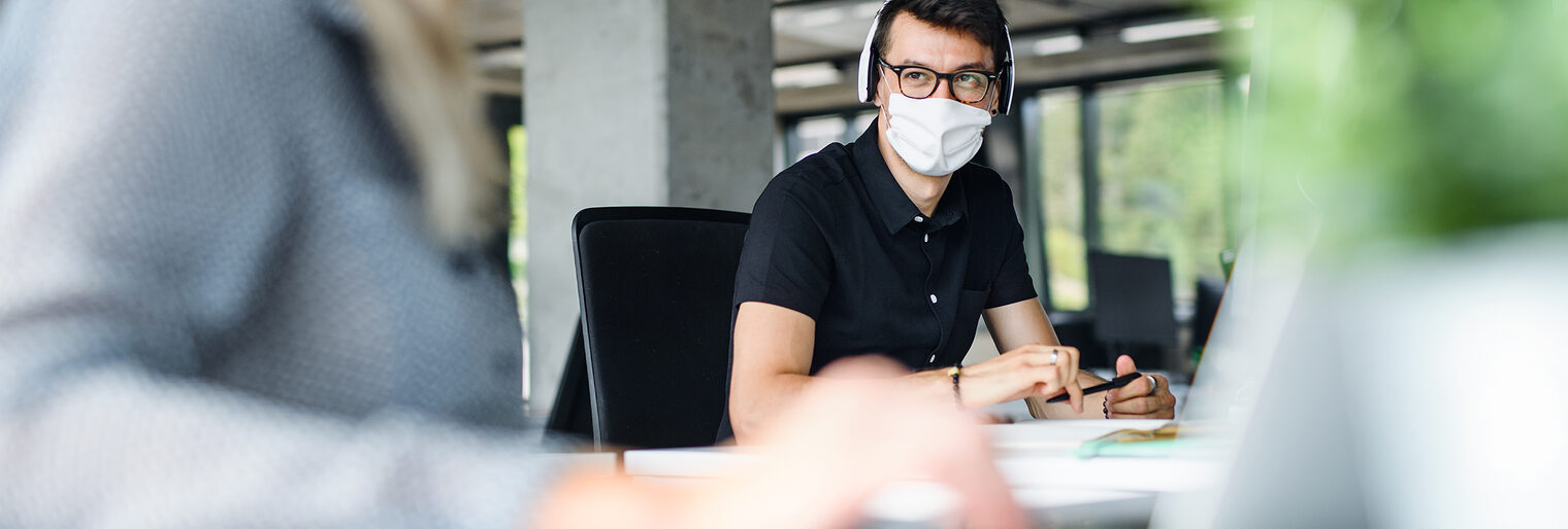 Mit Maske bzw. Mund-Nase-Bedeckung im Gespräch im Büro. Bild: Halfpoint / stock.adobe.com