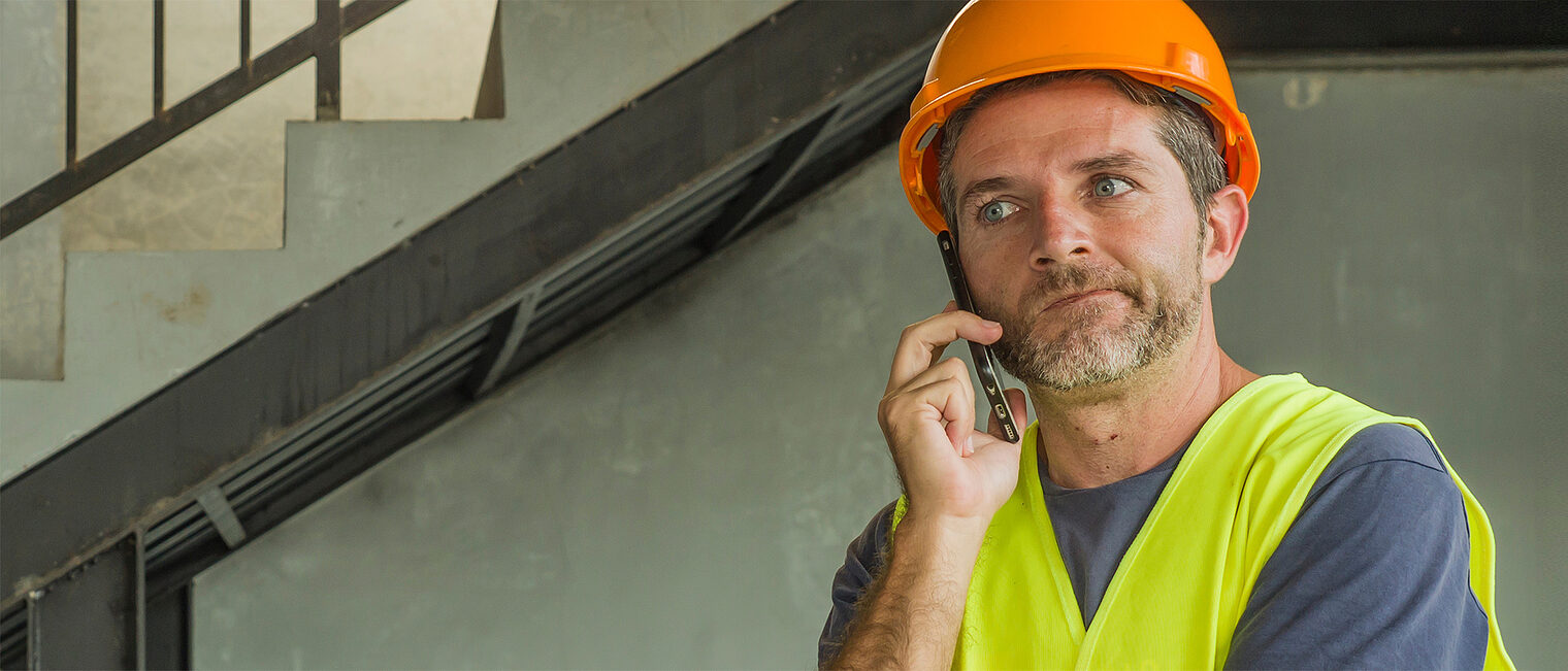 Unglücklich aussehender Bauhandwerker mit Schutzhelm am Handy. Bild: 