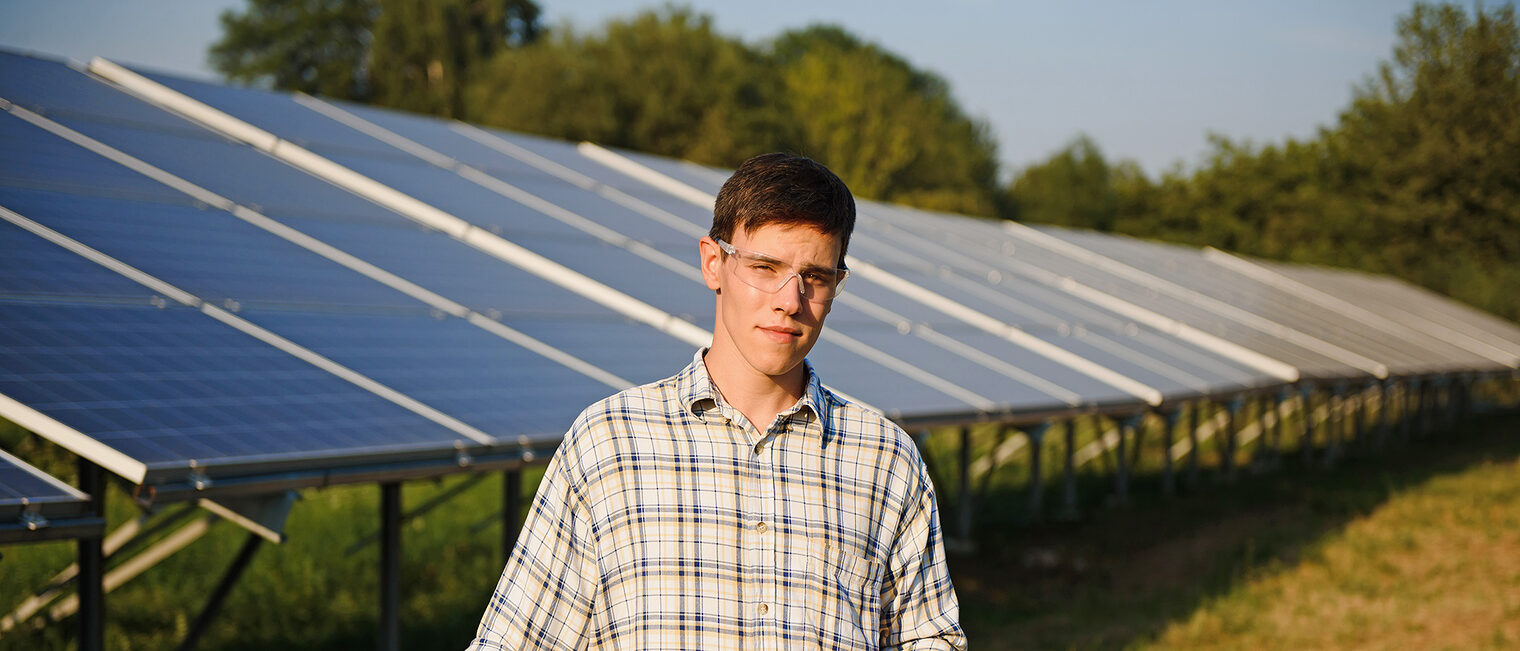 Junger Mann vor einer Solaranlage. Bild: stock.adobe.com / Serhii
