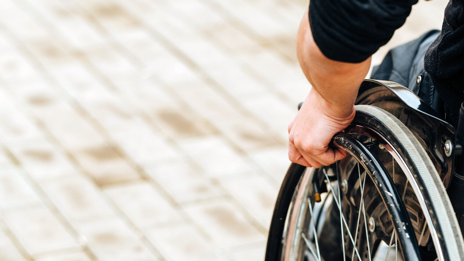 Close-up of male hand on wheel of wheelchair during walk in park. He holds his hands on the wheel. Schlagwort(e): wheelchair, wheel, invalid, disability, handicap, hand, care, disabled, person, chair, man, people, concept, handicapped, male, young, rehabilitation, health, patient, business, physical, closeup, injury, accessibility, sitting, medical, paralysis, healthcare, assistance, paralyzed, help, work, disable, desk, impairment, medicine, detail, equipment, agreement, teamwork, mobility, connection, collective, indoors, armchair, paraplegic, problem, pavement, therapy