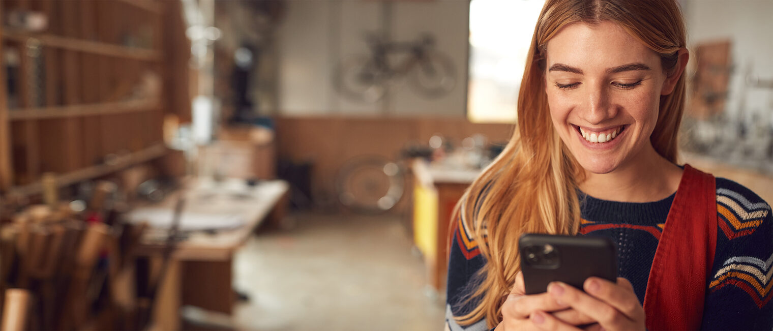 Lächelnde Handwerkerin mit Smartphone in einer Werkstatt. Bild: Monkey Business / stock.adobe.com