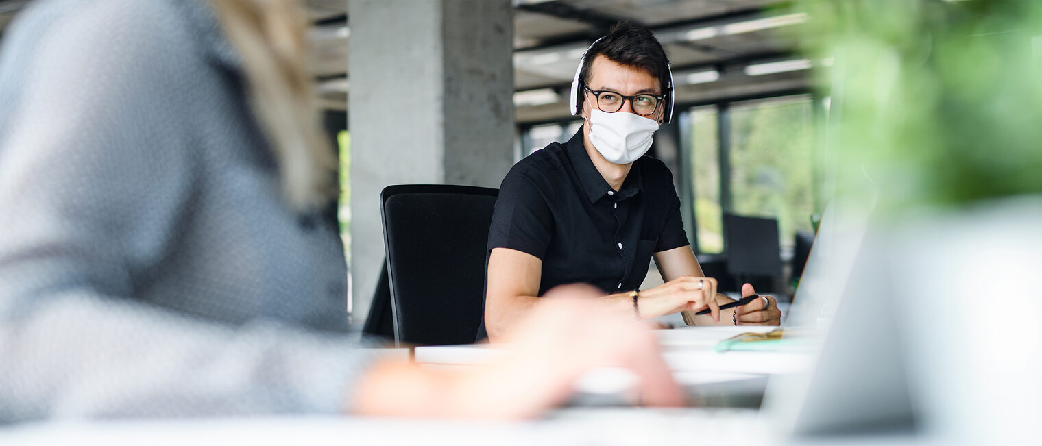 Mit Maske bzw. Mund-Nase-Bedeckung im Gespräch im Büro. Bild: Halfpoint / stock.adobe.com