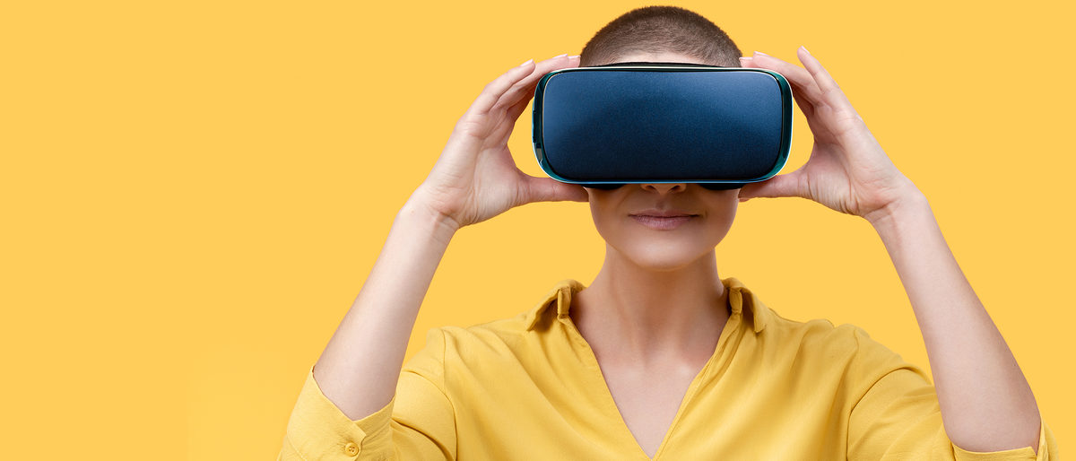 Young woman in her 30s using virtual reality goggles. Woman wearing VR headset isolated over yellow banner. VR experience concept. Schlagwort(e): vr, virtual, reality, goggles, woman, headset, experience, technology, background, banner, web banner, panoramic, panorama, digital, isolated, wearable, tech, goggle, wearing, google, googles, glasses, gadget, ar, holding, hand, 3d, future, concept, header, fun, young, studio shot, yellow, yellow background, one person, one young woman only, millennial, space, innovation, gear, vision, visual, simulation, device, relax, entertainment, virtuality