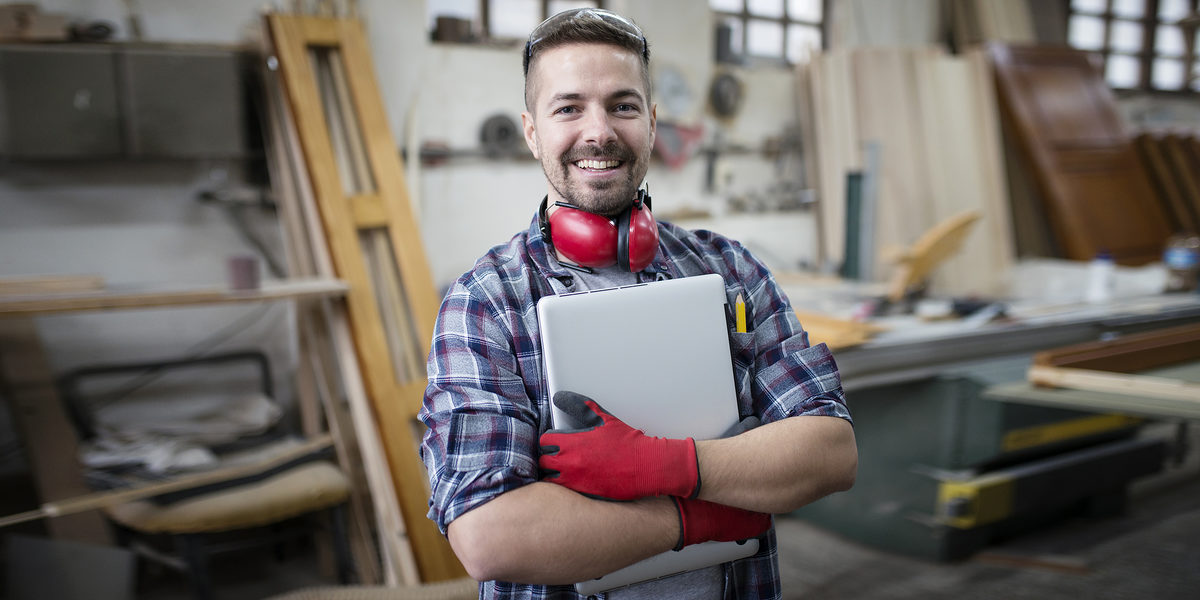 Portrait of experienced architect designer holding laptop computer in workshop. Schlagwort(e): caucasian, carpentry, glasses, carpenter, occupation, worker, machine, people, workshop, manufacturing, working, wood, equipment, operating, safety, industry, factory, skill, interior, job, woodworker, craftsmanship, workplace, handmade, handicraft, wooden, tool, woodworking, man, construction, professional, plank, craftsman, woodwork, business, work, manual, craft, architect, blueprint, project, papers, documents, tablet, computer, idea, creativity, creative, design, designer