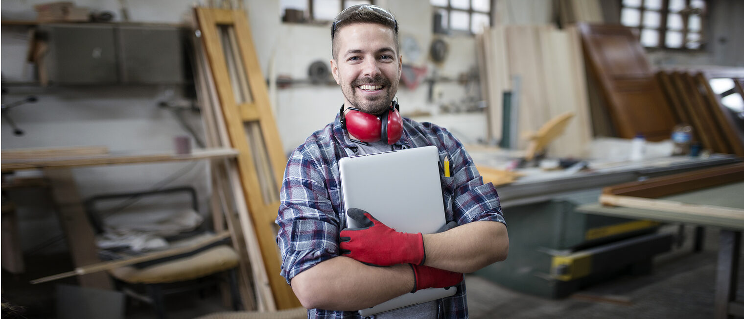 Portrait of experienced architect designer holding laptop computer in workshop. Schlagwort(e): caucasian, carpentry, glasses, carpenter, occupation, worker, machine, people, workshop, manufacturing, working, wood, equipment, operating, safety, industry, factory, skill, interior, job, woodworker, craftsmanship, workplace, handmade, handicraft, wooden, tool, woodworking, man, construction, professional, plank, craftsman, woodwork, business, work, manual, craft, architect, blueprint, project, papers, documents, tablet, computer, idea, creativity, creative, design, designer