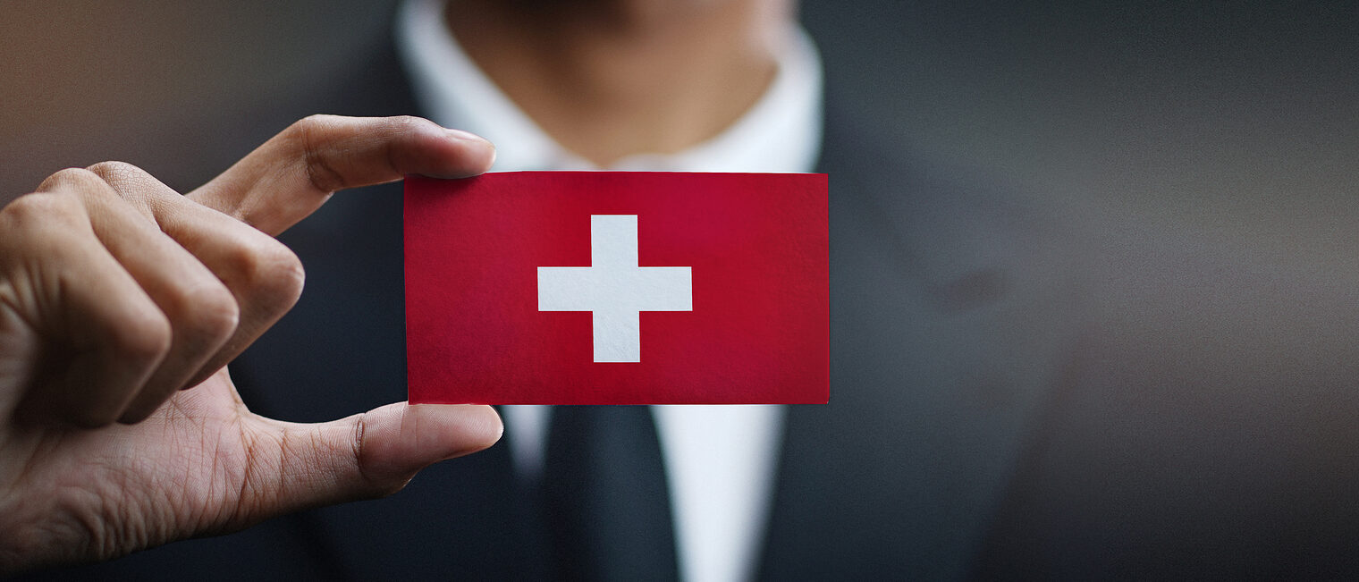 Businessman Holding Card of Switzerland Flag Schlagwort(e): business, businessman, card, concept, corporate, country, flag, hand, holding, man, nation, office, professional, showing, sign, suit, symbol, switzerland, swiss confederation, none, swiss, switzerland flag