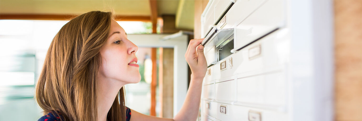 Junge Frau schaut in den Briefkasten. Bild: lightpoet / stock.adobe.com