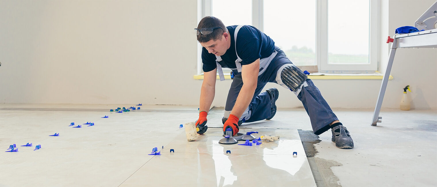 Handwerker verlegt Fliesen. Bild: stock.adobe.com / Liubomir