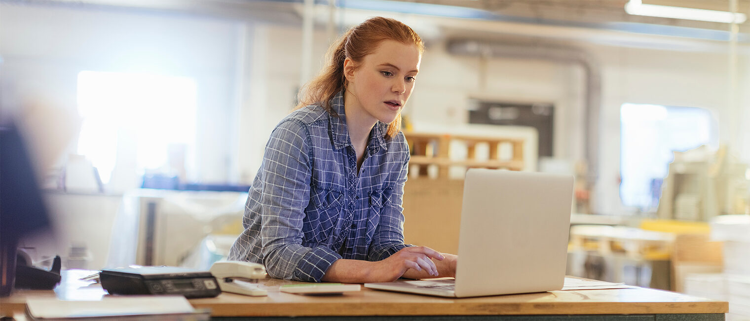 Junge Frau arbeitetin einer Werkstatt an einem Notebook. Bild: stock.adobe.com / Geber86