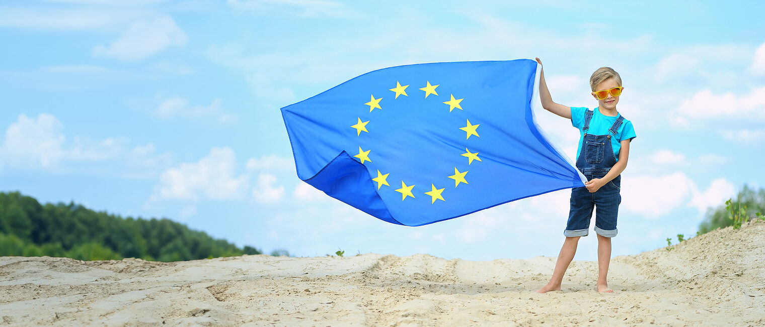 Junge mit Sonnenbrille hält eine Fahne der Europäischen Union. Bild: stock.adobe.com / Jacek (bearbeitet mit KI)