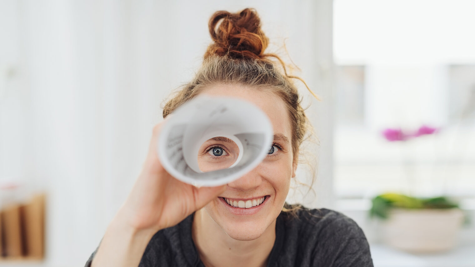Junge Frau schaut durch ein Fernrohr aus Papier und lacht. Bild: contrastwerkstatt / stock.adobe.com