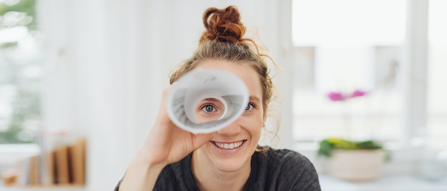 Junge Frau schaut durch ein Fernrohr aus Papier und lacht. Bild: contrastwerkstatt / stock.adobe.com