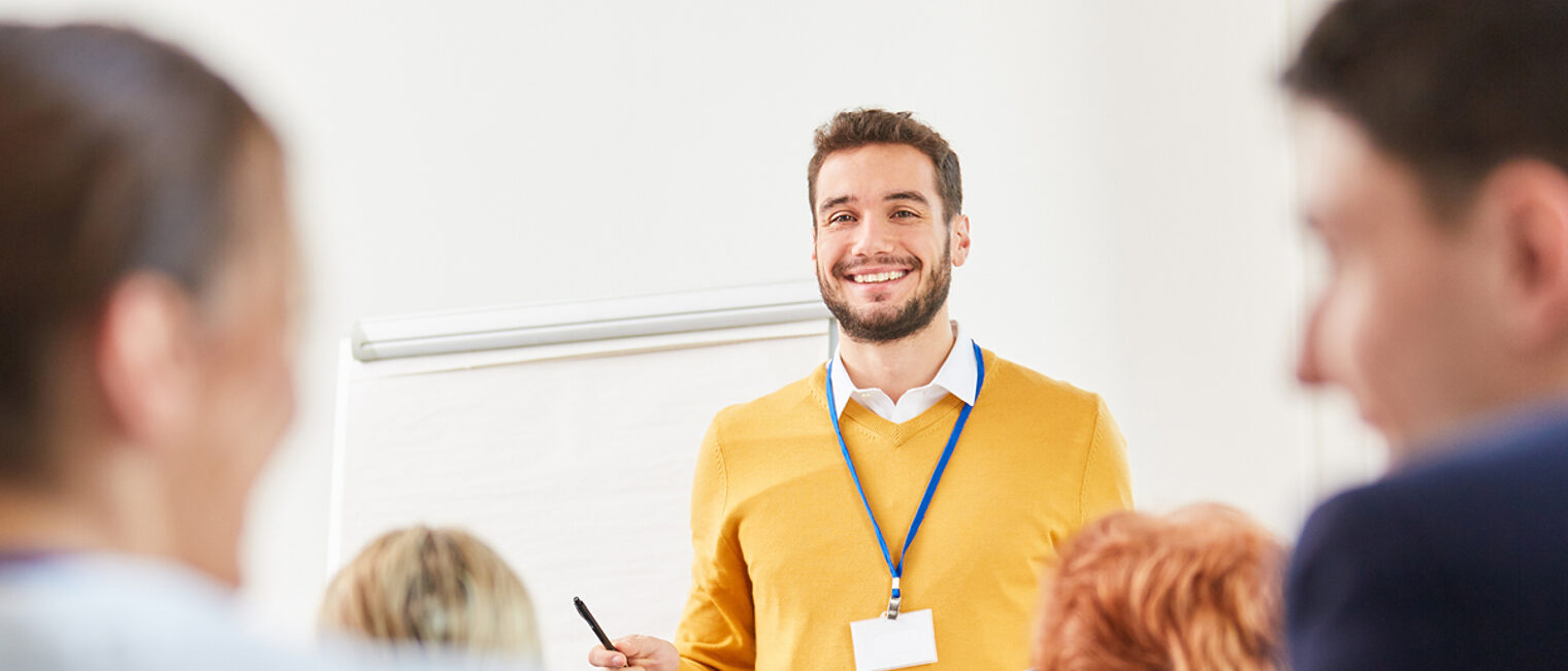 Ein Mann hält ein Referat. Fortbildungssituation: Ein lächelnder Dozent spricht in einem Seminar.