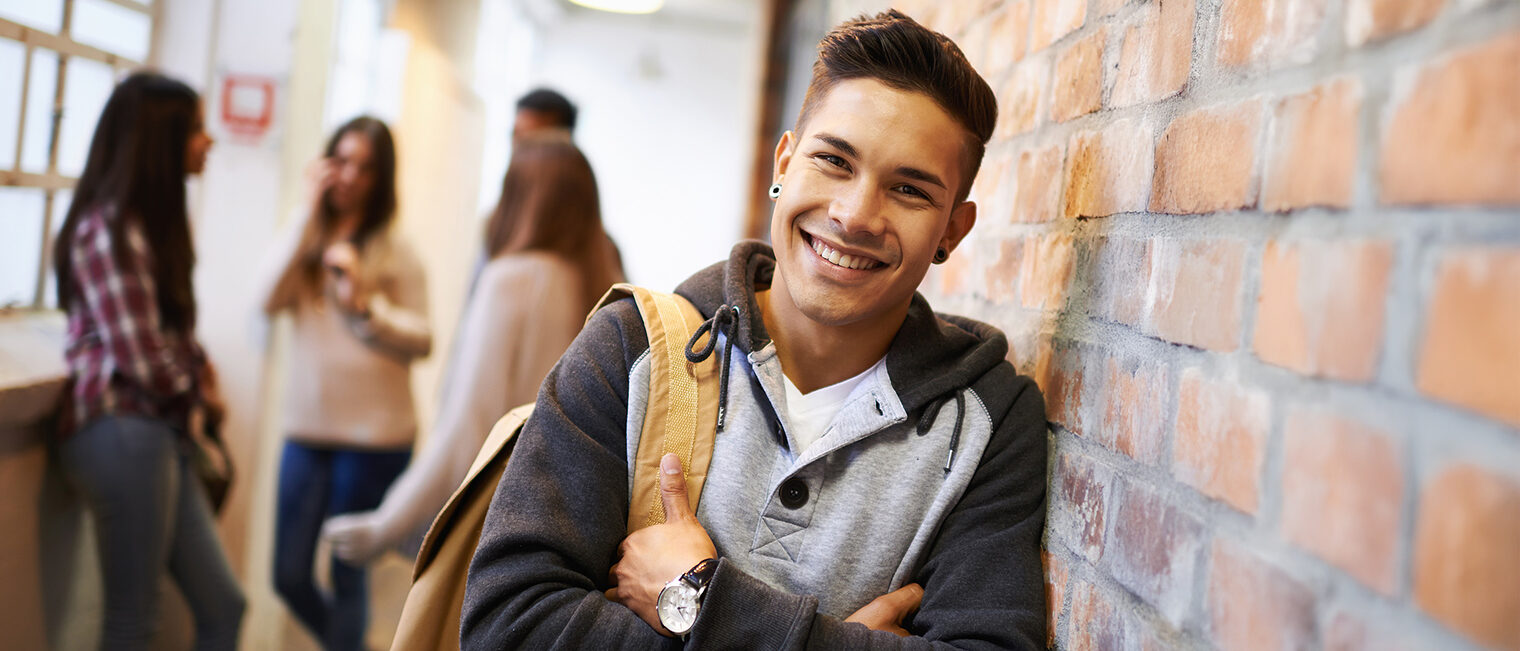 Ein junger Student lehnt in einer Schule an einer Wand.