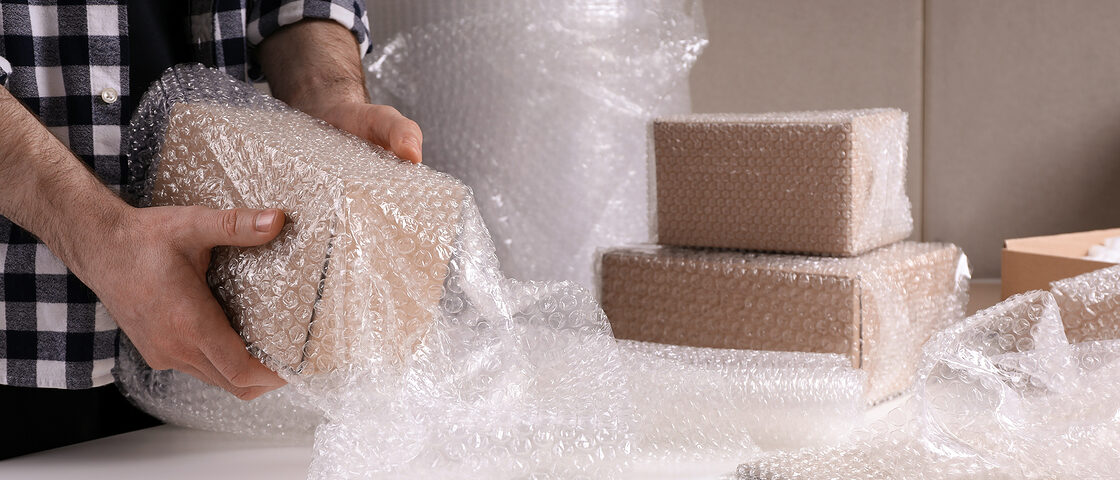 Ein Mann verpackt einen Karton mit Luftpolsterfolie.