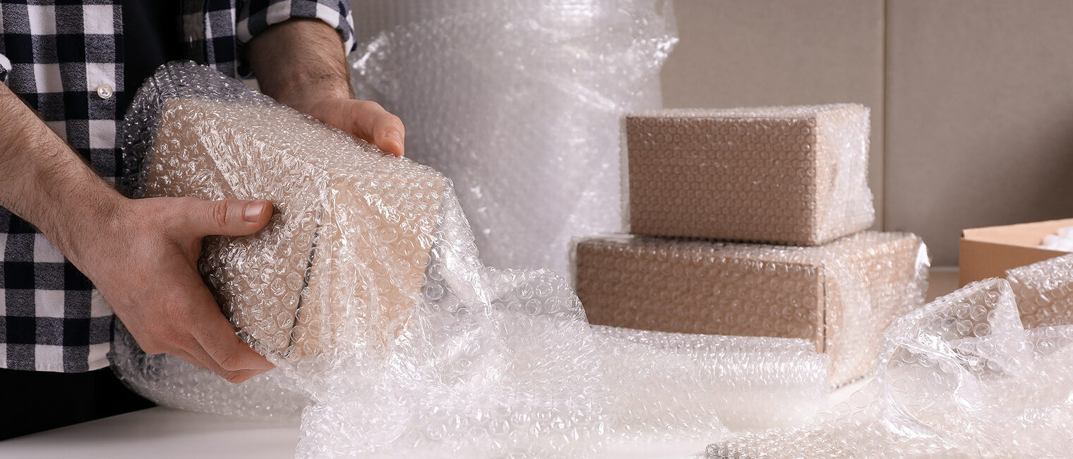 Ein Mann verpackt einen Karton mit Luftpolsterfolie. 