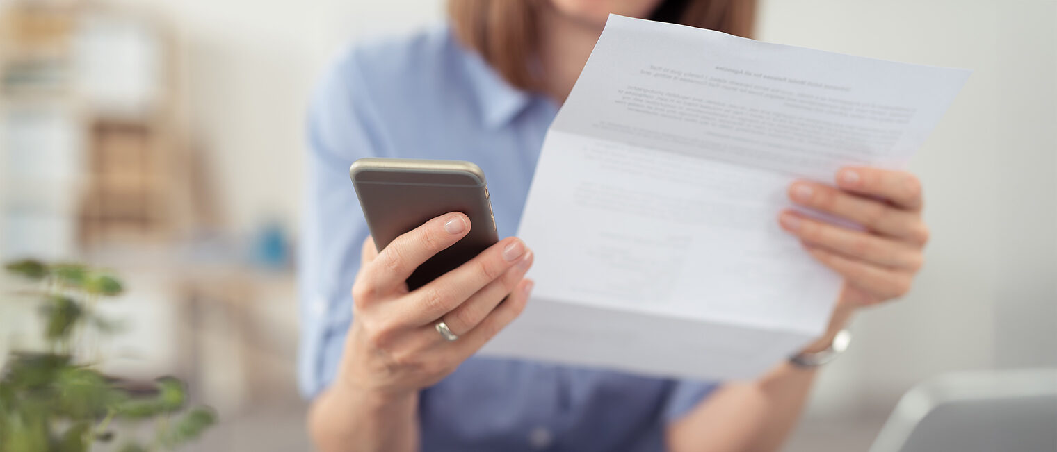 Eine Frau schaut auf einen Brief und tippt auf ihr Mobiltelefon.