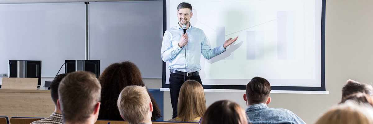 Handsome professor presenting his topic to students during lecture on university Schlagwort(e): lecture, lecturer, student, university, academy, classes, study, college, school, education, teacher, professor, conference, presentation, speech, business, audience, auditorium, lecture hall, higher education, attention, exam, learn, seminar, knowledge, group, listeners, coaching, training, man, young, handsome, people, color, panorama
