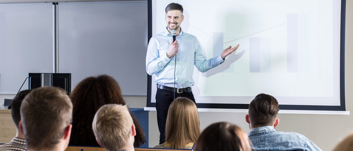 Handsome professor presenting his topic to students during lecture on university Schlagwort(e): lecture, lecturer, student, university, academy, classes, study, college, school, education, teacher, professor, conference, presentation, speech, business, audience, auditorium, lecture hall, higher education, attention, exam, learn, seminar, knowledge, group, listeners, coaching, training, man, young, handsome, people, color, panorama