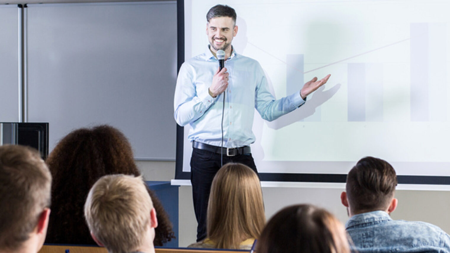 Handsome professor presenting his topic to students during lecture on university Schlagwort(e): lecture, lecturer, student, university, academy, classes, study, college, school, education, teacher, professor, conference, presentation, speech, business, audience, auditorium, lecture hall, higher education, attention, exam, learn, seminar, knowledge, group, listeners, coaching, training, man, young, handsome, people, color, panorama