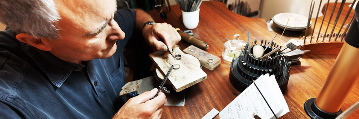 Senior man working at shaping a ring Schlagwort(e): adult, caucasian, chisel, close, closeup, face, goldsmith, grey, hair, hammer, hand, hands, holding, industry, jewelry, job, light, look, looking, male, man, mature, men, metal, note, one, paper, people, person, professional, ring, senior, serious, sitting, table, tool, trade, tradesman, work, working