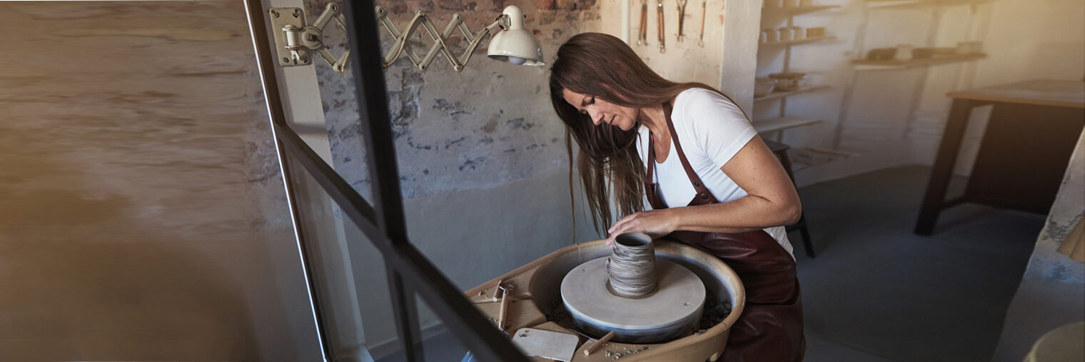 Female artisan sitting in her ceramic workshop using a tool to shape a piece of clay turning on a pottery wheel Schlagwort(e): adults, artisan, artist, bowl, caucasian, ceramics, clay, copy space, craft, crafting, craftsperson, creative, creativity, entrepreneur, equipment, expertise, female, handmade, hands, hobby, inside, inspiration, lens flare, looking through, making, one, person, potter, pottery, sculpting, shaping, sitting, skill, small business, spinning, studio, tool, turning, vase, wet, wheel, white, window, woman, working, workshop