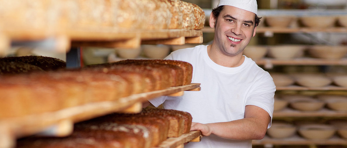 Bäcker in der Backstube mit einem Wagen voller Brote. Bild: contrastwerkstatt / fotolia.com