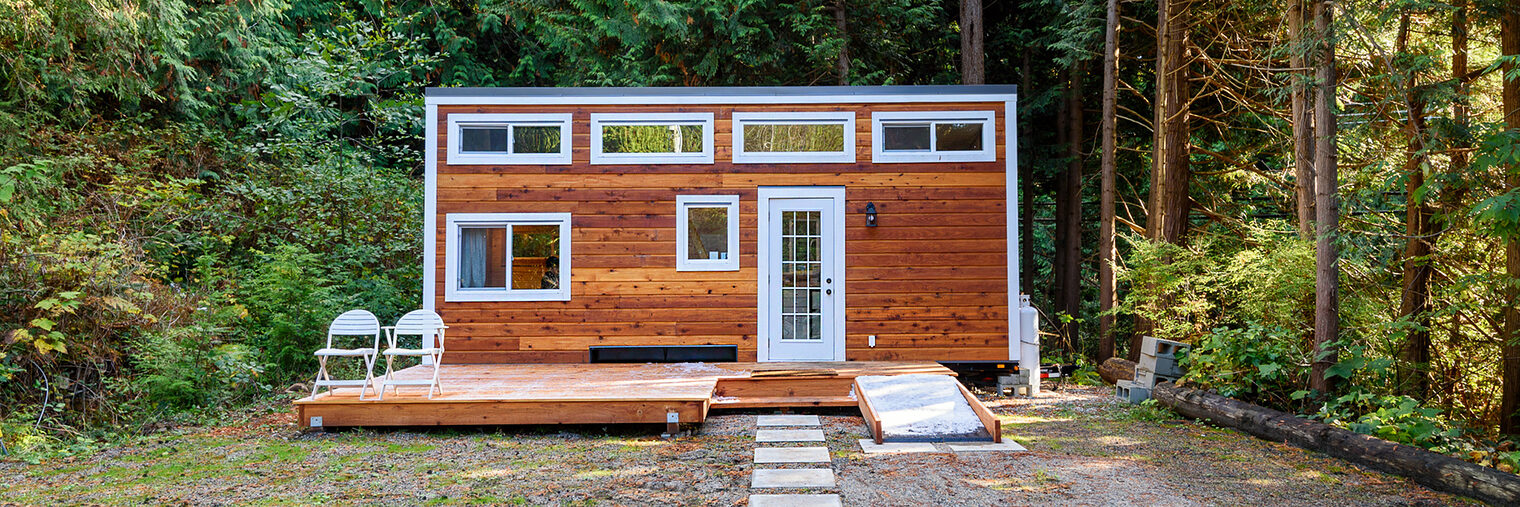 Small wooden cabin house. Exterior design. Schlagwort(e): architecture, bench, building, cabin, cottage, countryside, design, exterior, forest, garden, home, house, idyllic, landscape, log, minimalist, modern, nature, new, patio, rural, rustic, small, sunny, tiny, vacation, window, wood, wooden